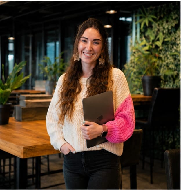 Nata van Houdt standing with a laptop under her arm in a plant-filled office